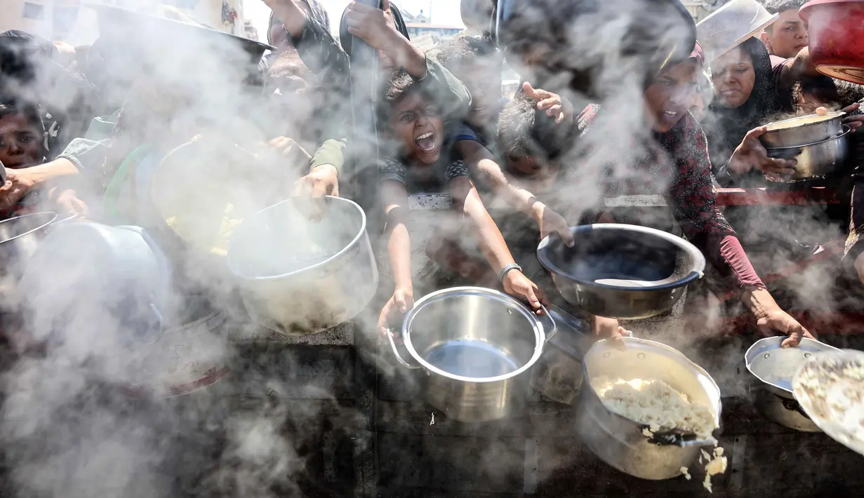Warga Palestina yang mengulurkan panci kosong di depan dapur umum untuk menerima makanan matang di Kota Gaza pada 23 Agustus 2025. (Foto : AFP/Omar AL-QATTAA)